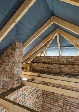 Attic space of a building under construction with wooden beams of a roof structure and brick walls. Real estate development concept.