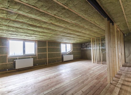 Construction and renovation of big light spacious empty room with oak floor, walls and ceiling insulated with rock wool, heating radiators under low attic windows and wooden frame for future walls.