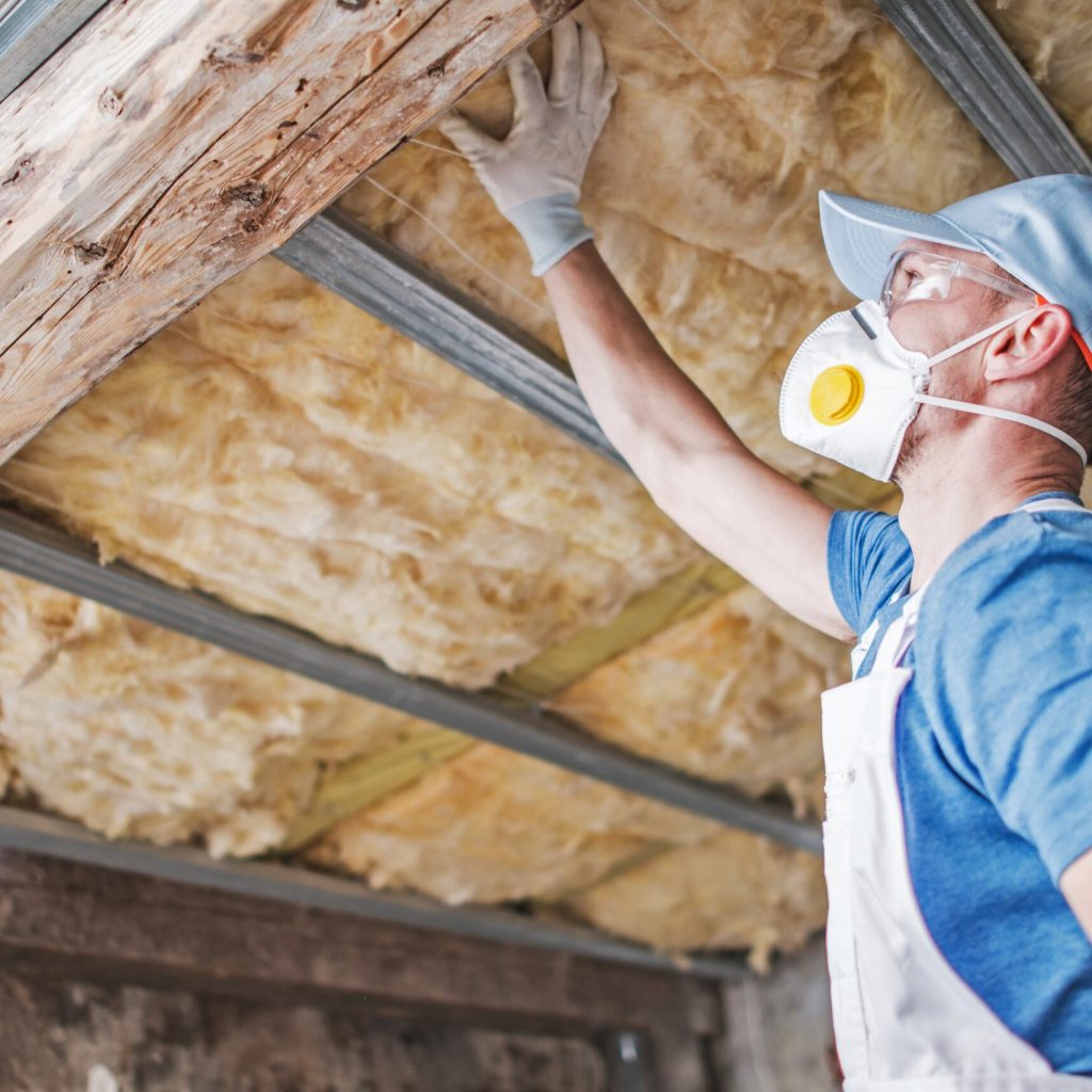 Old Roof Insulation. Caucasian Construction Worker in His 30s Inspecting Aged Roof and Mineral Wool Insulator.