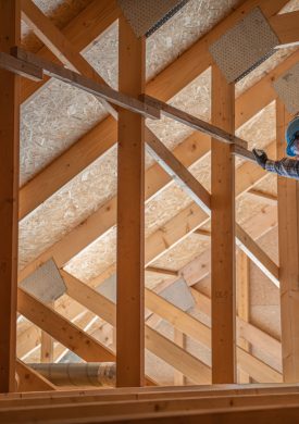 Caucasian Construction Contractor Worker in His 30s Checking on Wooden Attic and Roof Structure. Industrial Theme