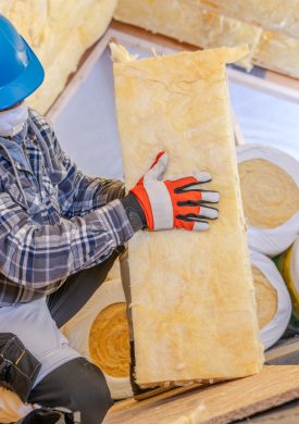 A construction worker is carefully installing insulation materials in a residential attic, wearing safety gear and ensuring proper fit for energy efficiency.